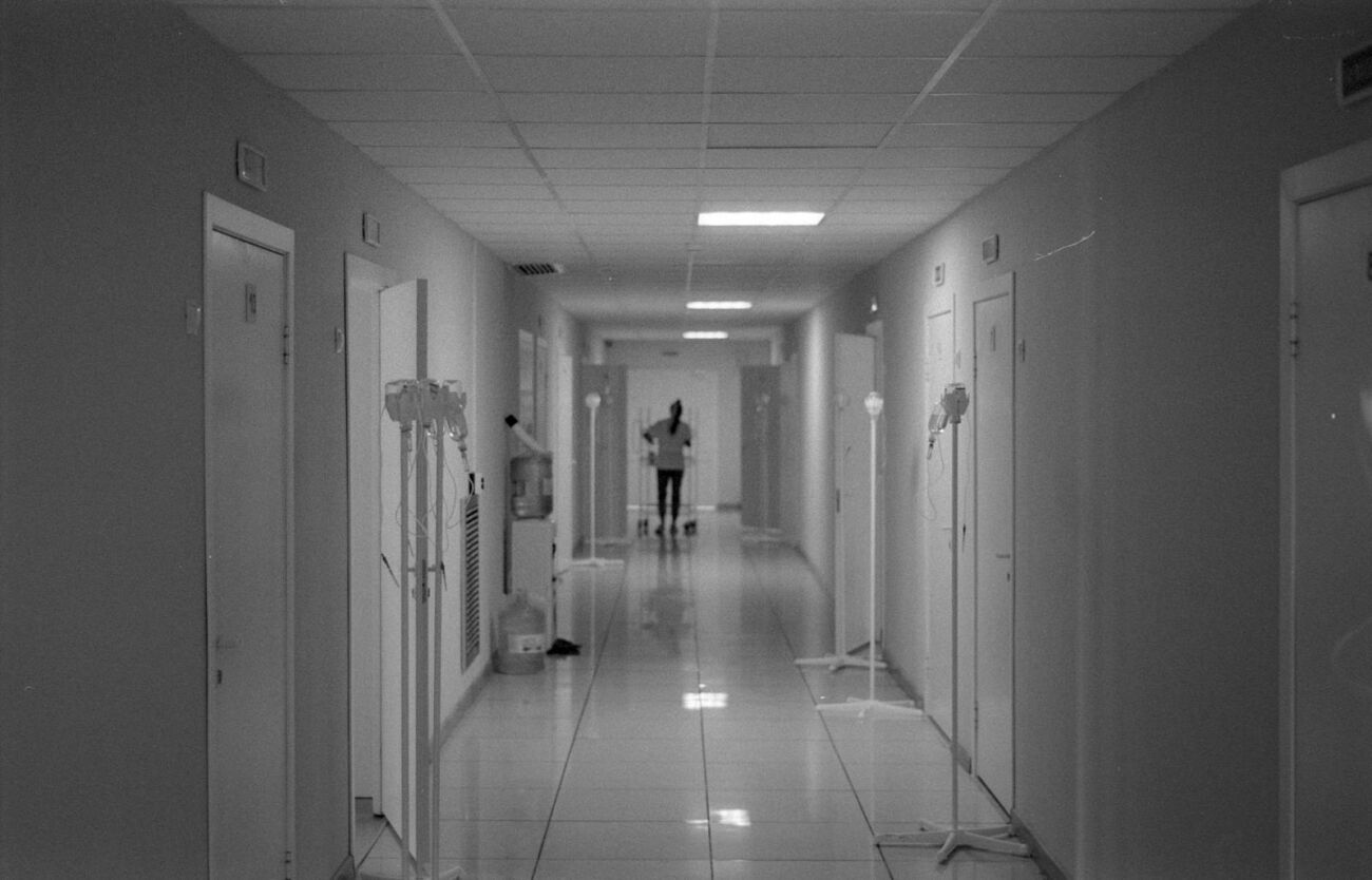 Monochrome image of a hospital hallway with a nurse in the background, highlighting healthcare environment.